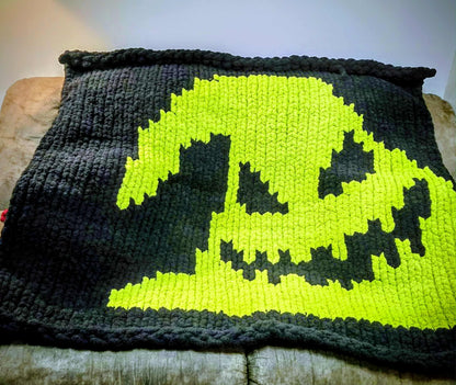 Knitted blanket with an Oogie Boogie face design on a couch surface