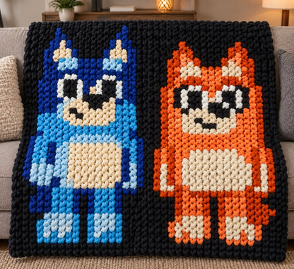 A chunky knit throw blanket featuring two pixel-art characters, a blue creature on the left and an orange fox on the right, set against a black background, draped over a sofa in a living room setting.