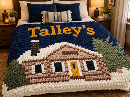 A chunky knit blanket on a bed in a bedroom setting, featuring a cabin design with the text 'Talley's' in yellow.
