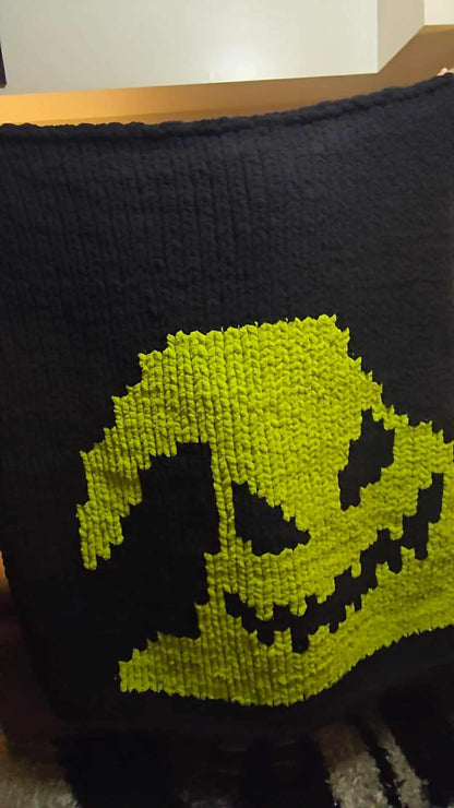 Black and green knitted blanket with a Oogie Boogie face design on a wooden surface.