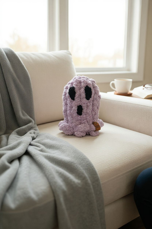 Plush ghost toy on a white couch with a light gray blanket and a cup in the background.
