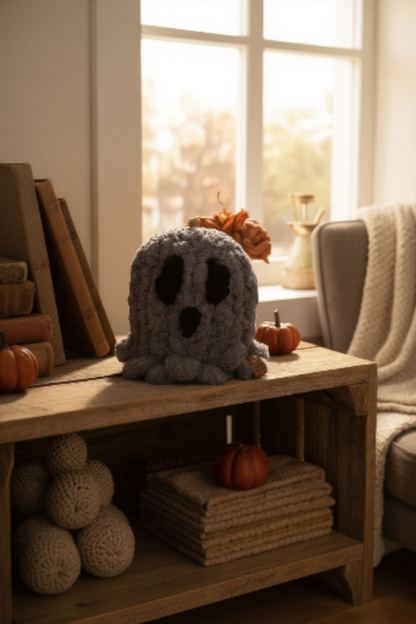 Gray knitted ghost toy on a wooden table with pumpkins and books in a cozy room.