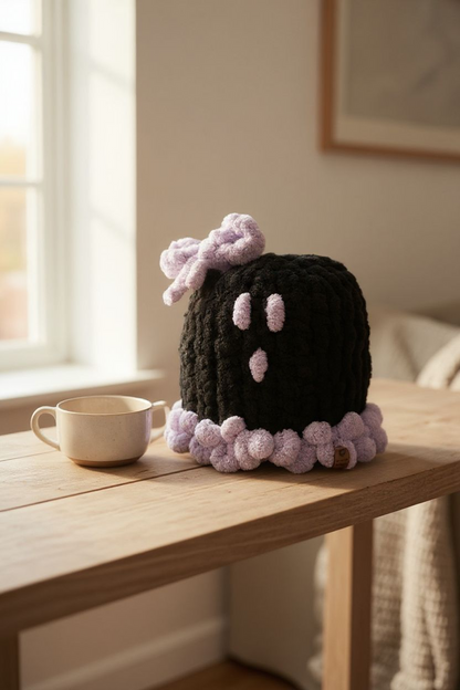 Knitted black and pink Large ghost with a bow on a wooden table near a window.