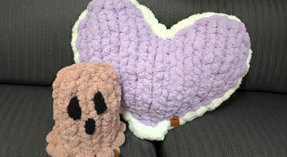 Heart-shaped pillow and ghost plush toy on a dark surface