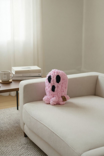 Pink plush ghost toy on a beige sofa with a neutral background